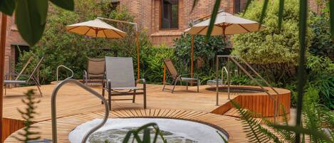 A wooden deck with a hot tub, two lounge chairs, and two umbrellas.