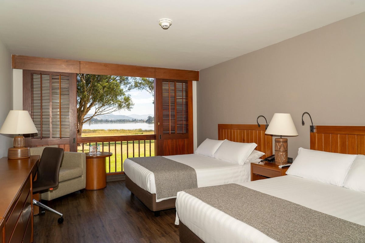 Habitación de hotel con dos camas, un escritorio, una silla y vistas a un lago.