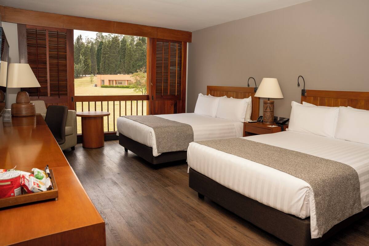 Habitación de hotel con dos camas, un escritorio y vistas al exterior.