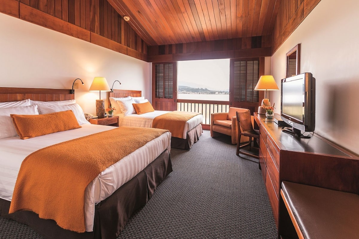 Habitación de hotel con dos camas, televisión, escritorio y vistas al exterior.
