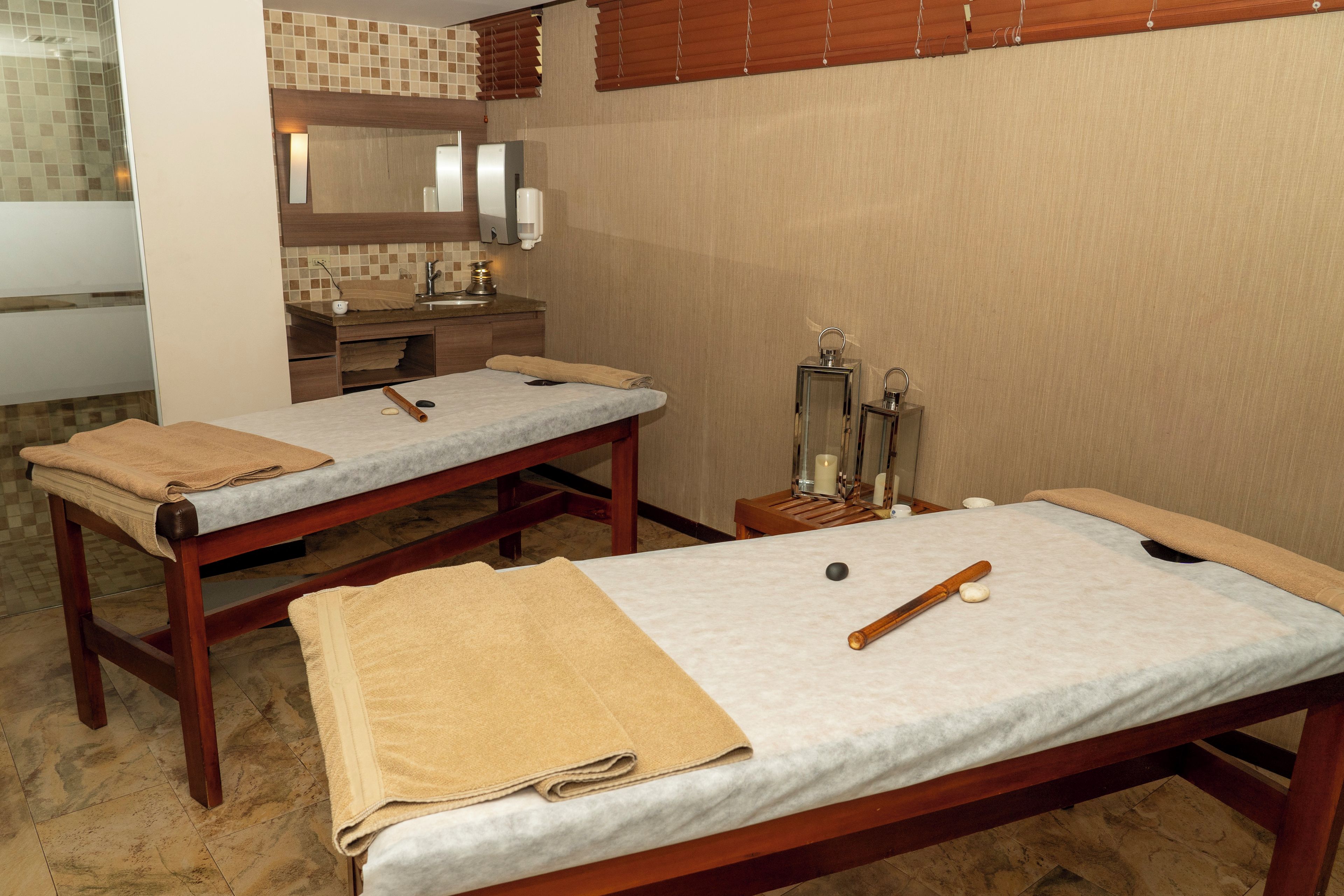 A spa room with two massage tables, towels, a wooden bench, a mirror, and a wall-mounted massage chair.