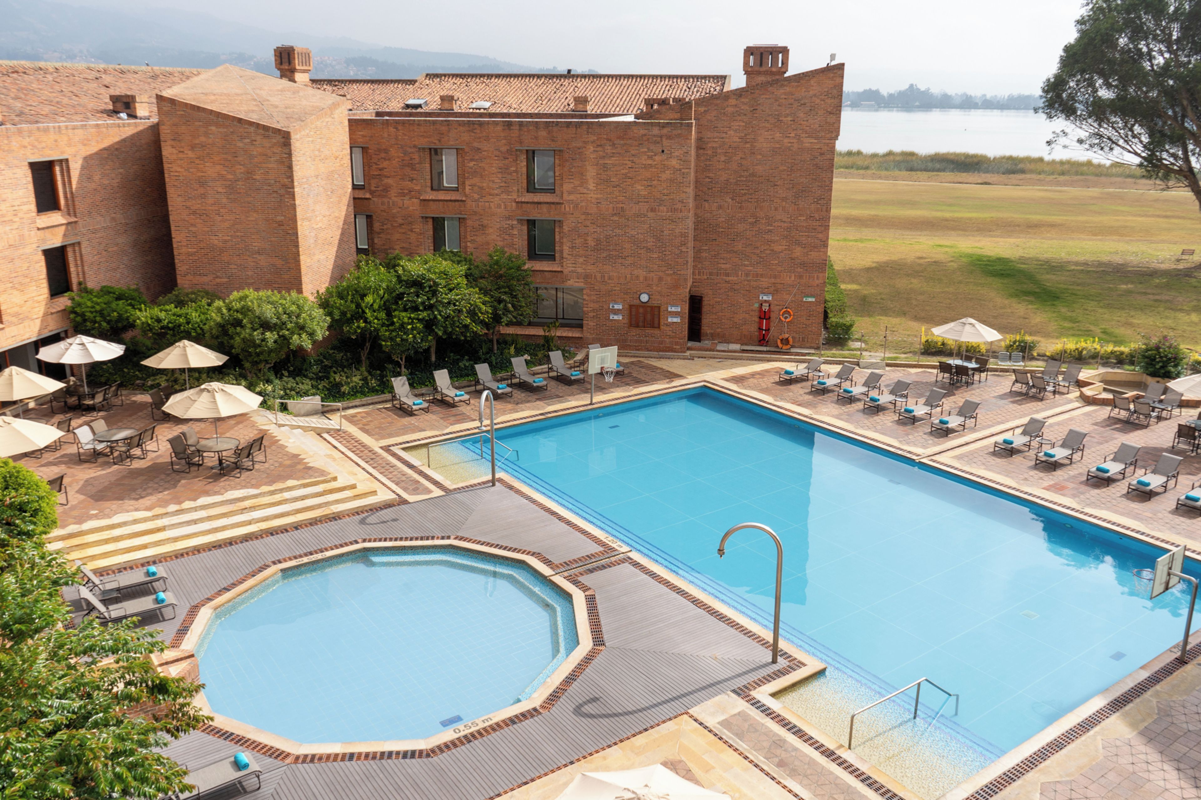 Ein Swimmingpool mit Liegestühlen und Sonnenschirmen, umgeben von einem Backsteinhaus mit Blick auf einen See.