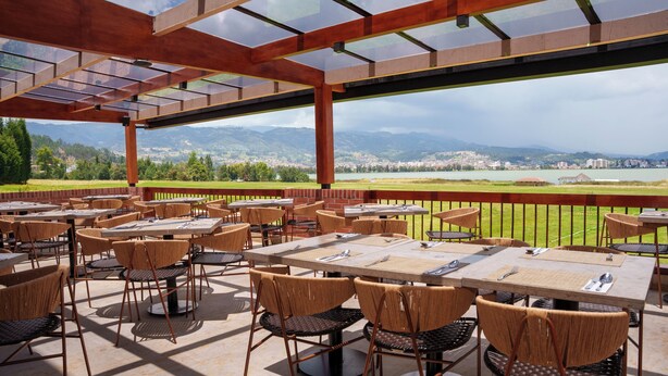 Un espace de restauration en plein air avec des tables et des chaises, un plafond en verre et une vue sur une ville et des montagnes en arrière-plan.