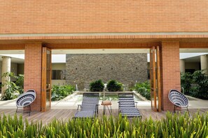 A modern building with a brick facade, a stone wall, and a pool area with lounge chairs. - Estelar Paipa Hotel Spa & Centro de Convenciones (Paipa)