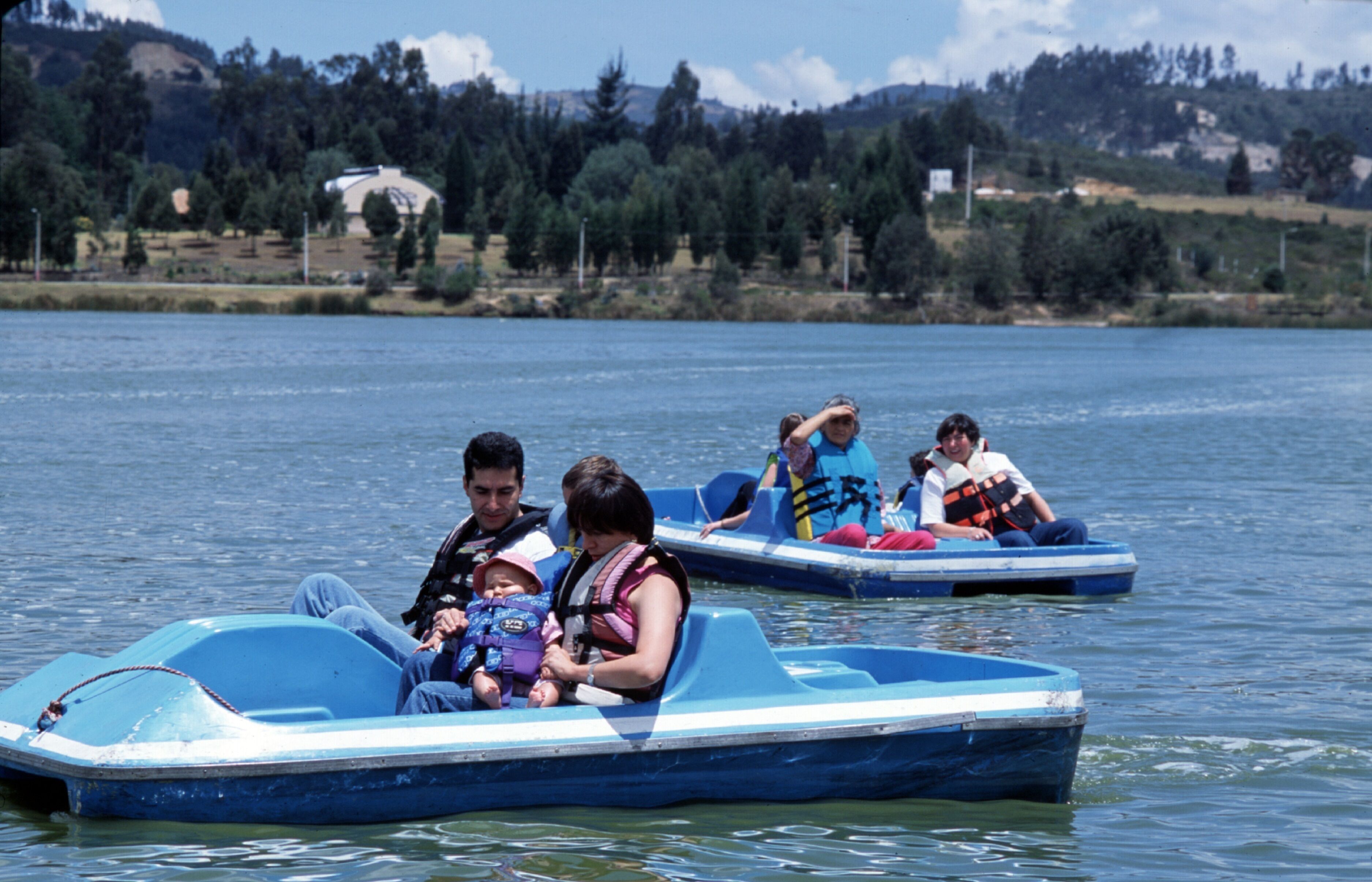 A group of people in a small blue boat on a lake with a forested hillside in the background.