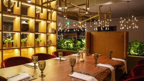 A restaurant with a long wooden table set for dining, red upholstered chairs, and a warm ambient lighting.