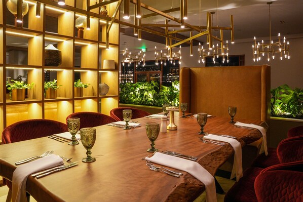Un restaurante con una larga mesa de madera dispuesta para comer, sillas tapizadas en rojo e iluminación ambiental cálida.