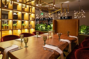Un restaurant dotĂ© dâune longue table en bois, dressĂ©e pour le repas, de chaises Ă lâassise rembourrĂ©e de tissu rouge et dâun Ă©clairage dâambiance chaleureux.