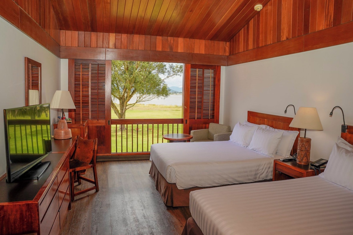 A hotel room with two beds, a television, a desk, and a view of a golf course.