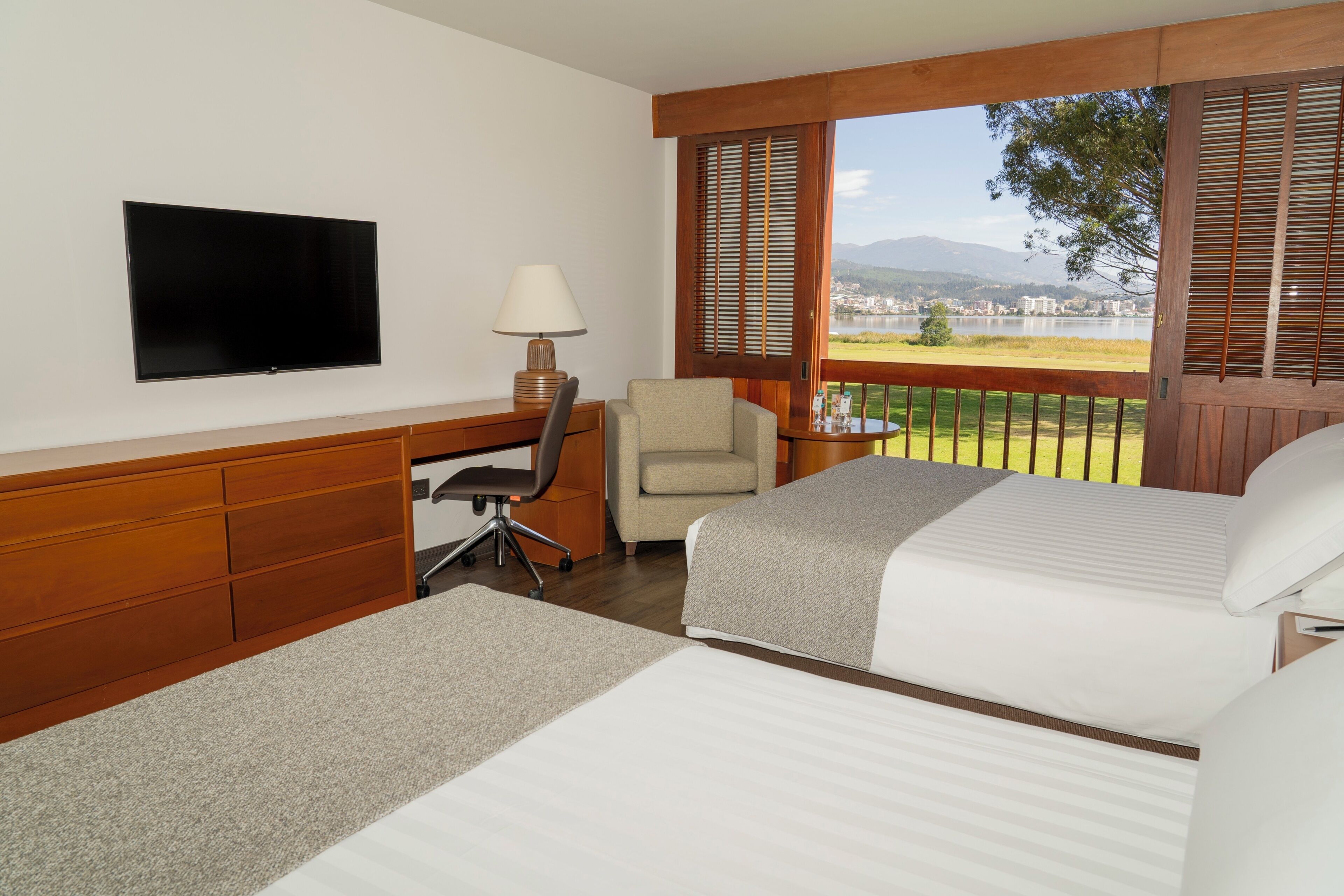 A hotel room with a bed, desk, chair, TV, and a balcony with a view.