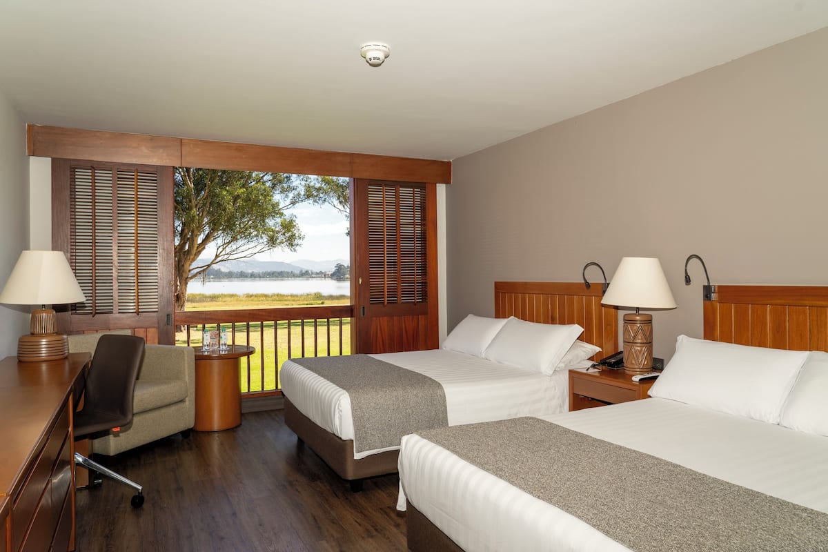 Una habitación de hotel con dos camas, un escritorio, una silla y vistas al exterior.