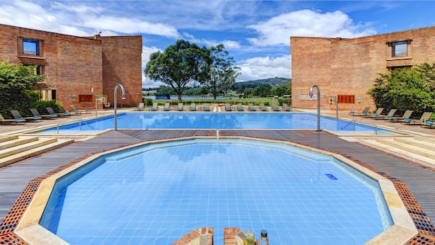 A rectangular swimming pool with a tiled deck, surrounded by lounge chairs and a brick building.