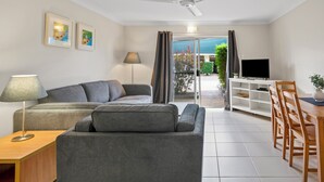 Una sala de estar moderna con un sofá gris, una mesita de madera y un televisor sobre un mueble blanco.