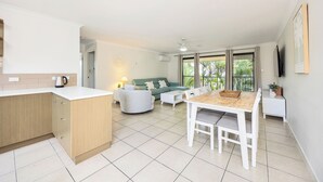 Una cocina moderna con una encimera blanca, horno empotrado y comedor con mesa de madera y sillas blancas.