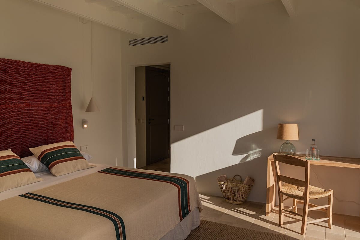 A bedroom with two beds, a desk, a chair, a lamp, and a basket.