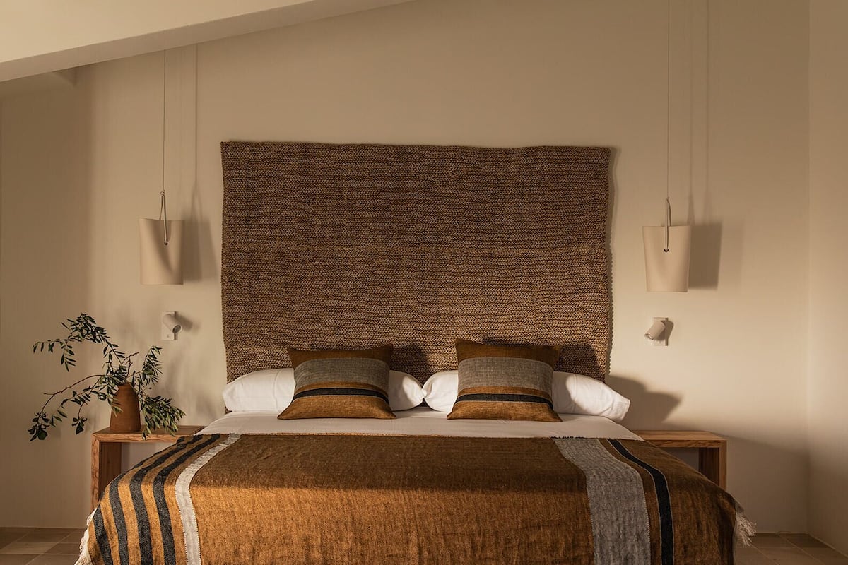 A bedroom with a large woven headboard, two bedside tables, a bed with a striped blanket, and a potted plant.