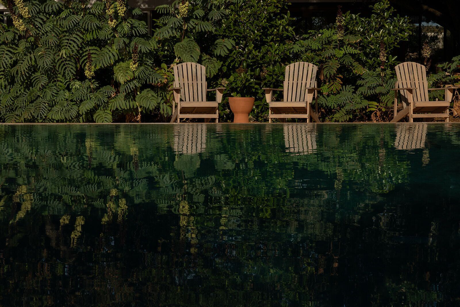 Ein Pool mit drei Adirondack-Stühlen und einem großen Terrakotta-Pflanzgefäß.
