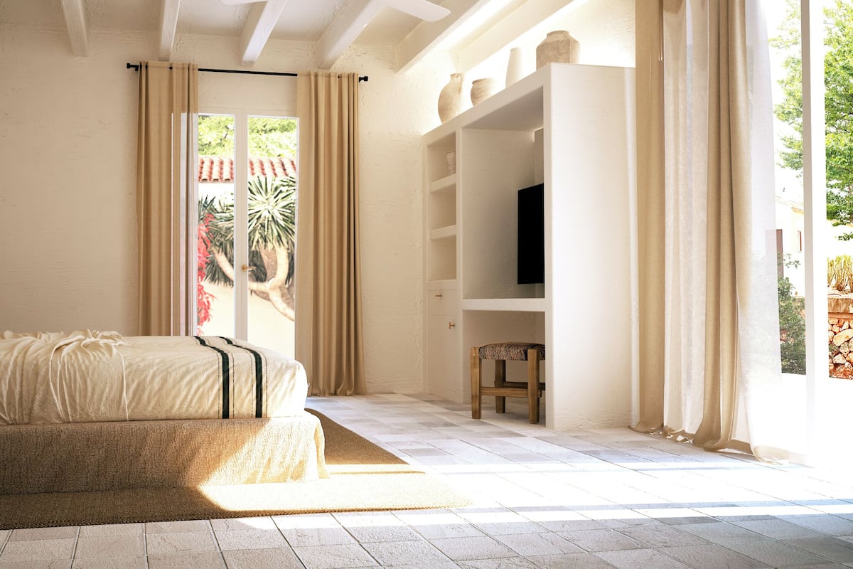 A bedroom with a bed, bedside table, lamp, and a view of the outdoors.