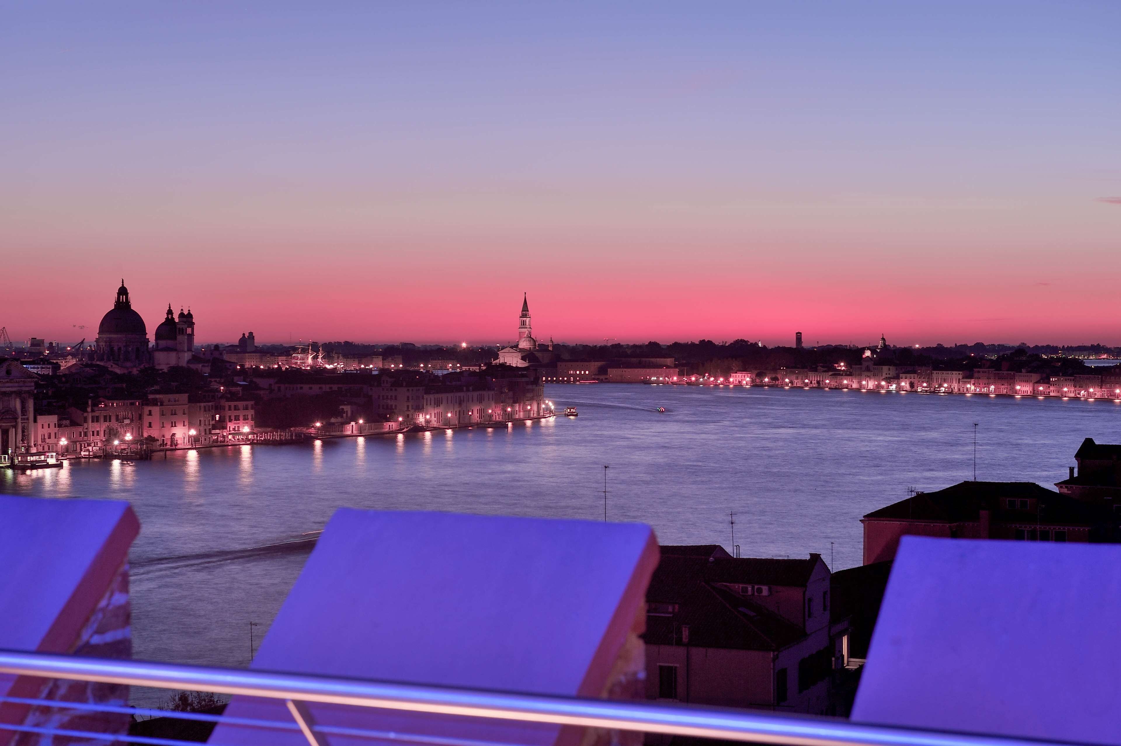 A cityscape at dusk with a river, illuminated buildings, and a prominent church spire.