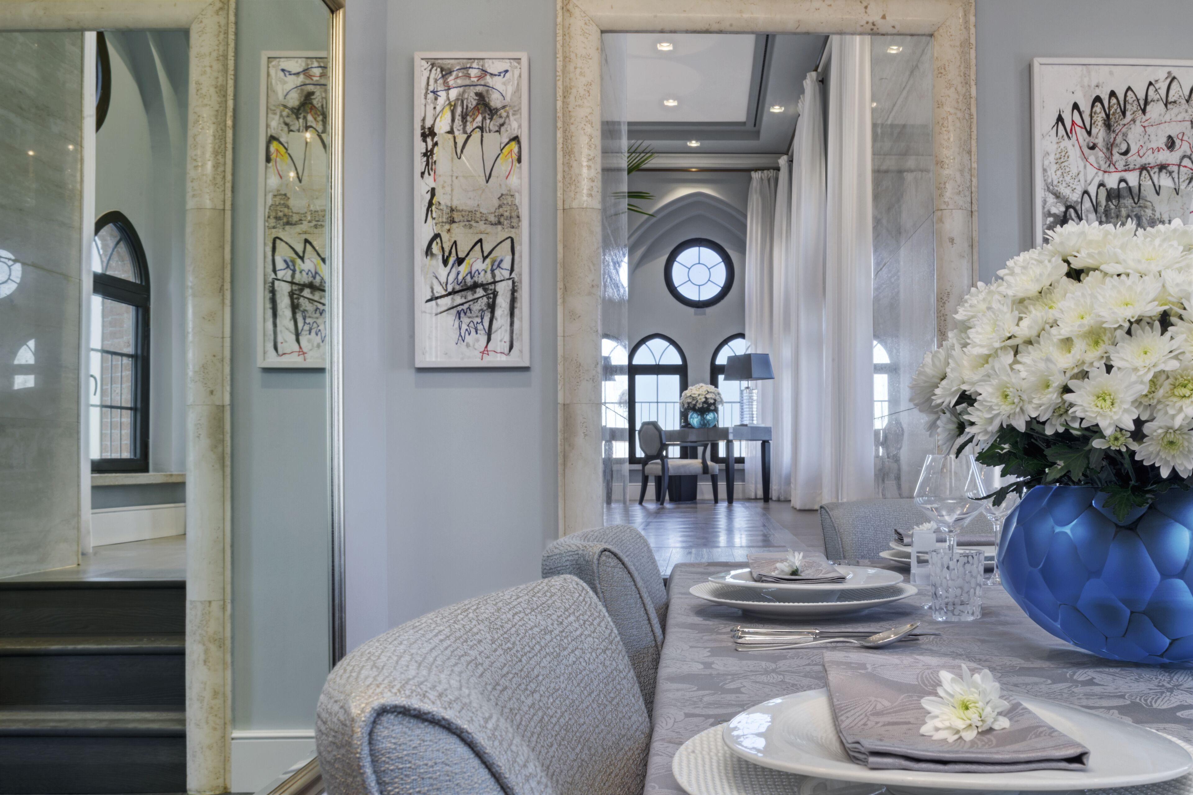 En spiseplads med et marmorbord dækket til fire personer, en stor blå vase med hvide blomster og abstrakt kunst på væggene.