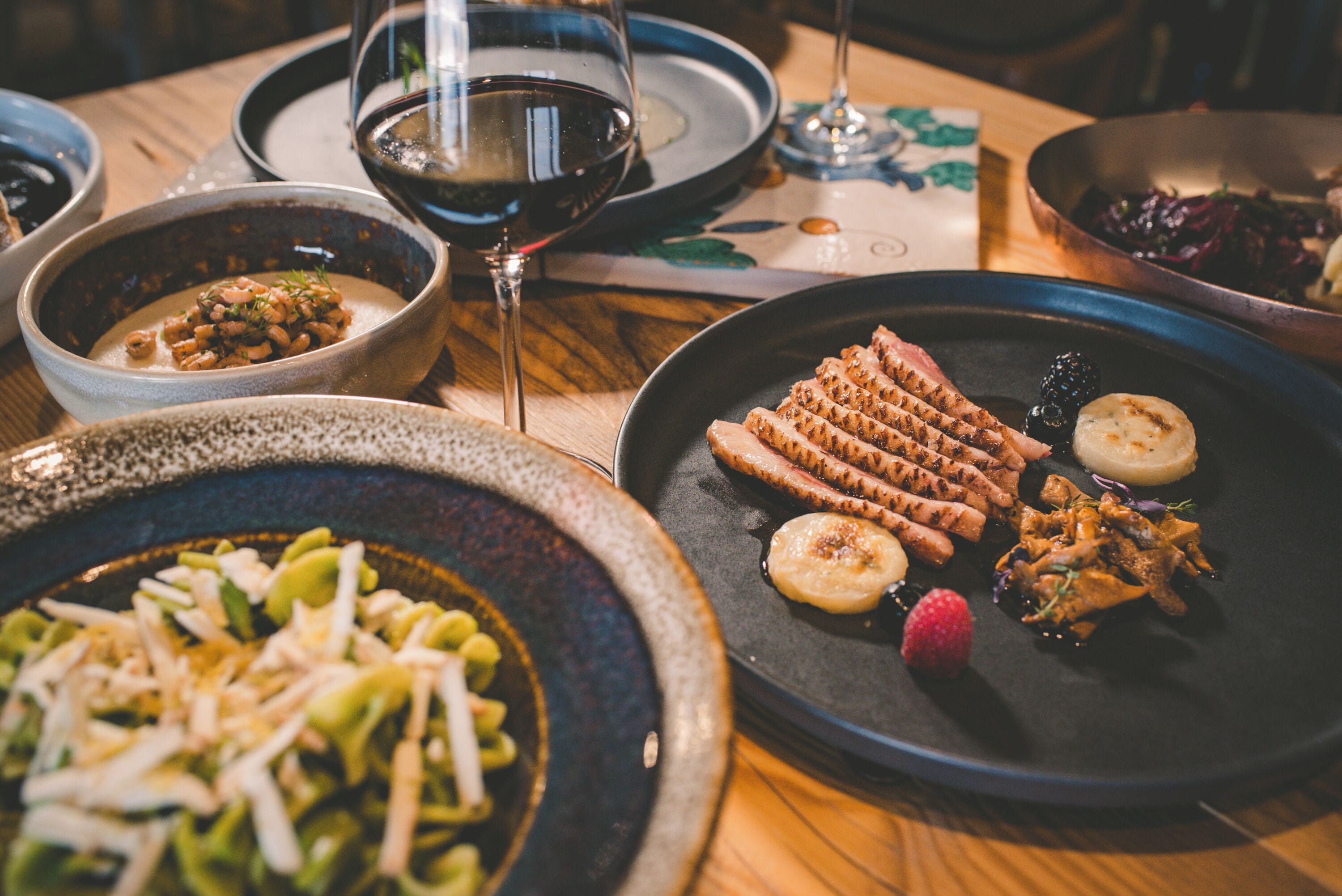A table with various dishes, including grilled meat, vegetables, and a bowl of beans.