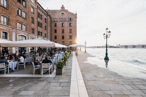 A waterfront dining area with outdoor seating, a brick building in the background, and a lamp post. - Hilton Molino Stucky Venice (Venice)