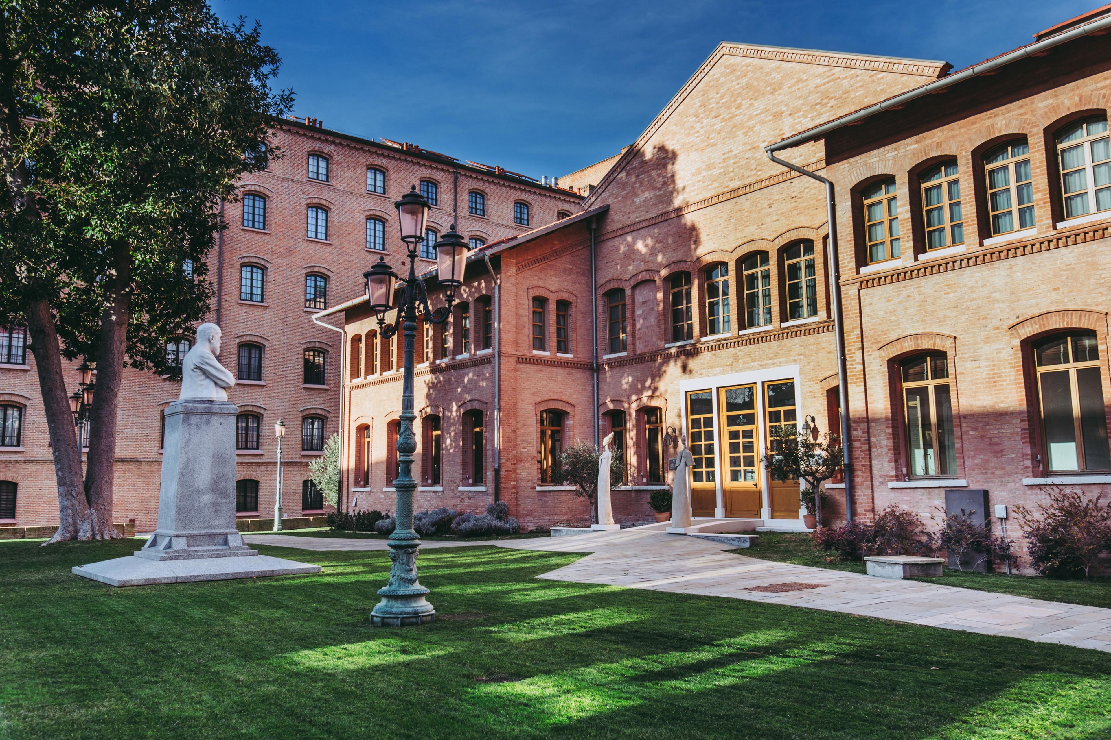 A courtyard with a statue, a building with multiple windows, and a well-maintained lawn.