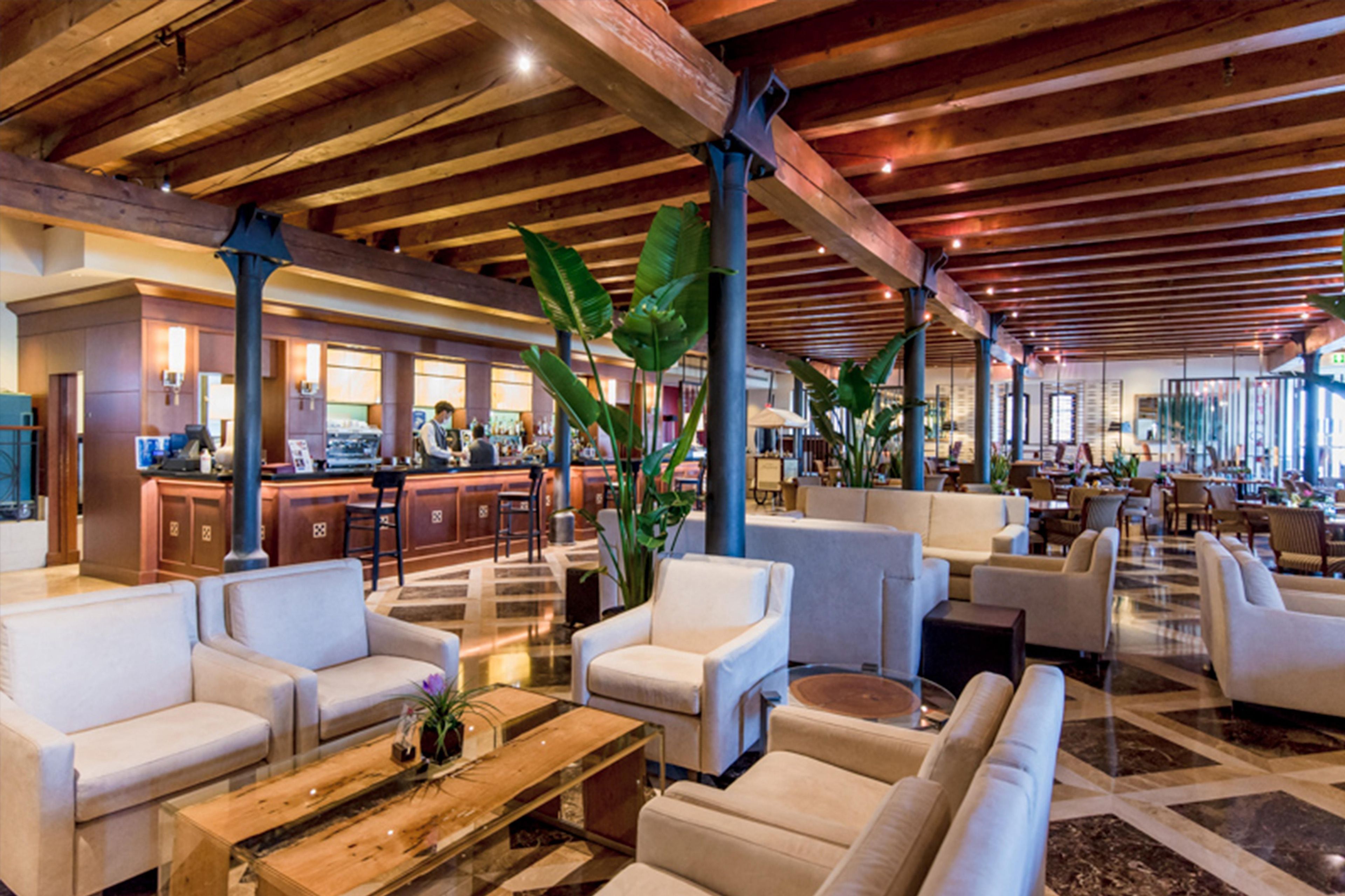 A spacious lobby with a high ceiling, wooden beams, and a mix of seating arrangements including sofas and armchairs.