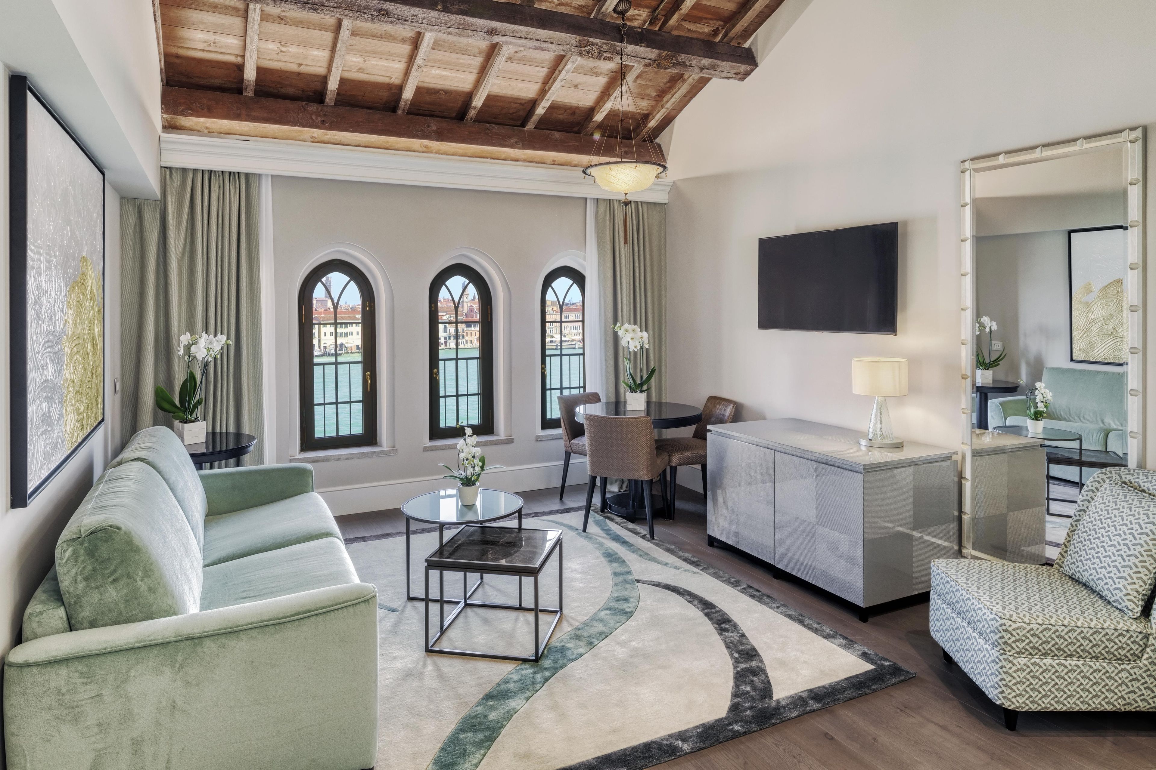 A spacious living room with a high ceiling, a dining area, and a view of a canal through arched windows.