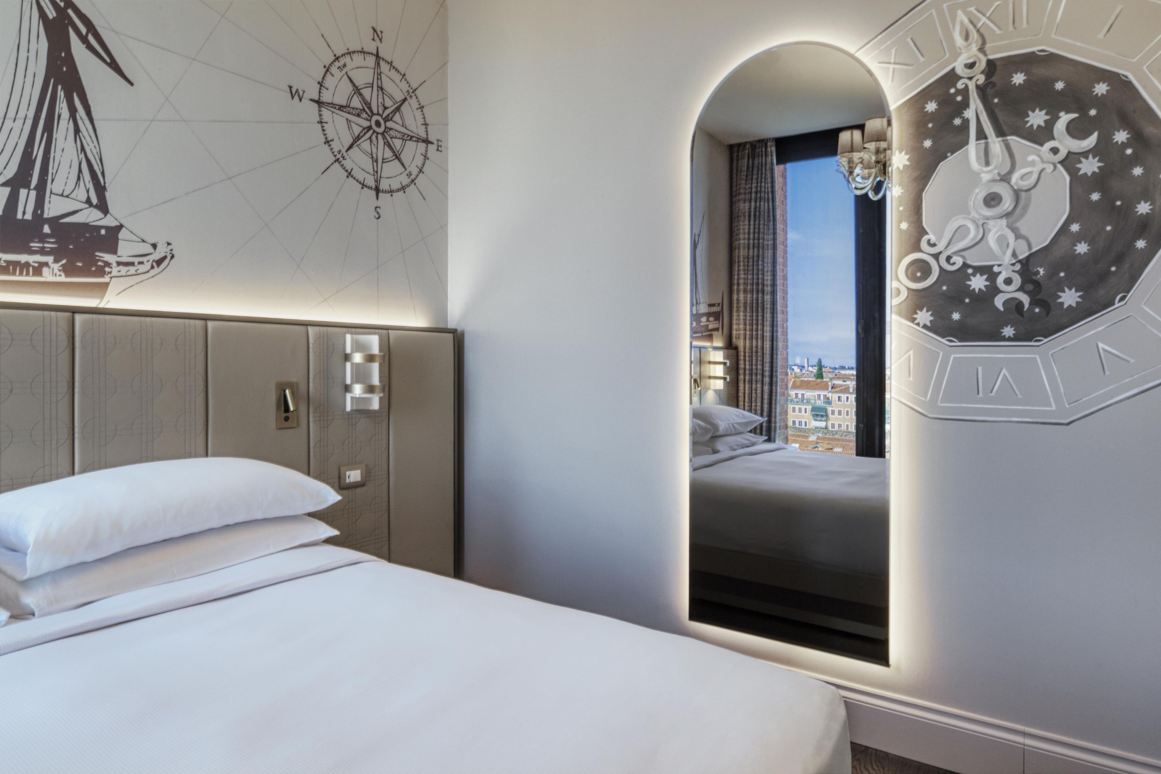 A hotel room with a bed, a wall clock, and a window with a city view.