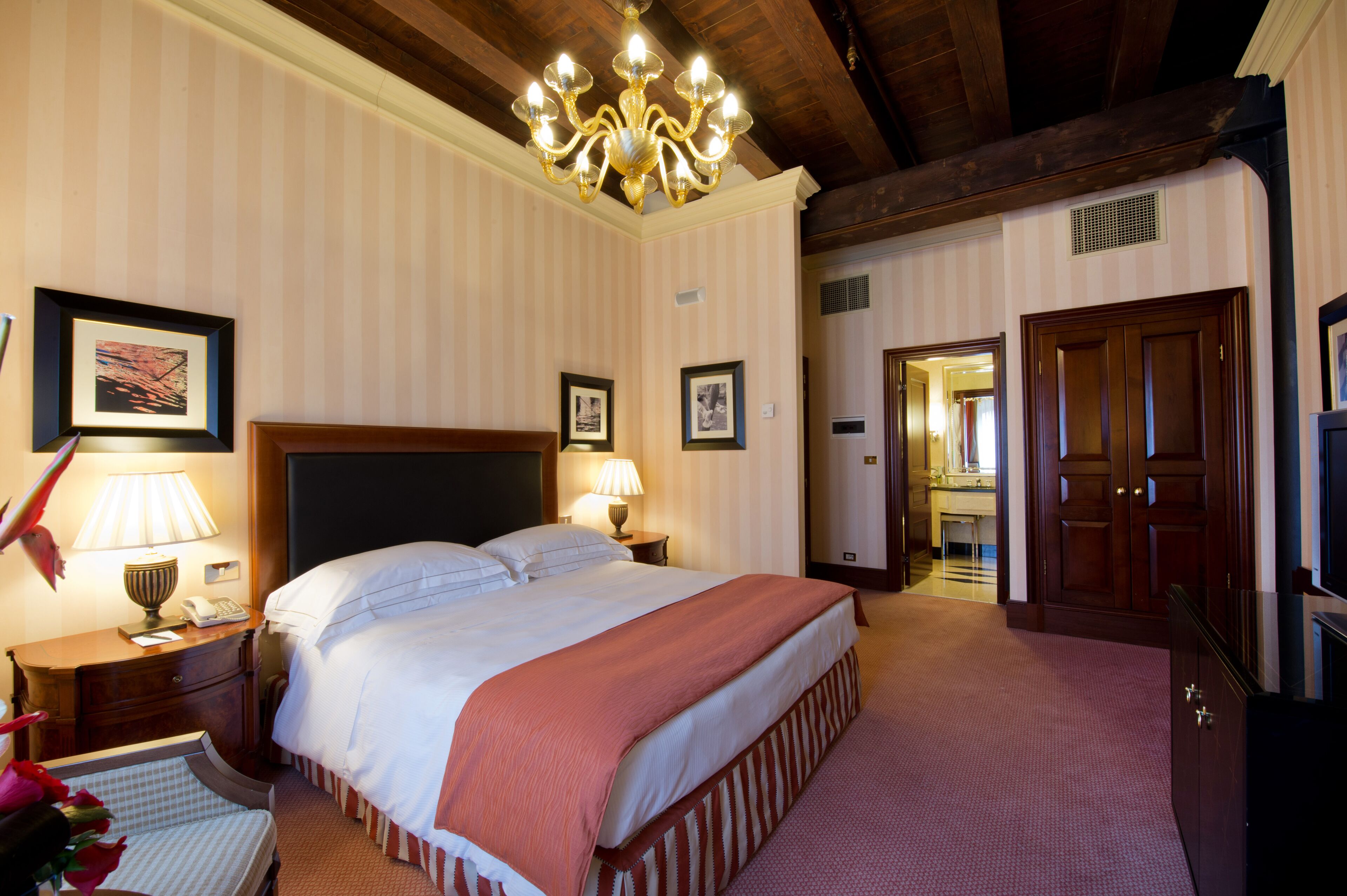 A hotel room with a large bed, a chandelier, a wooden door, and a framed picture on the wall.