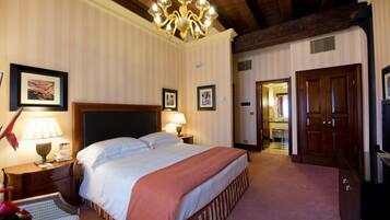 A hotel room with a large bed, a chandelier, a wooden door, and a framed picture on the wall.