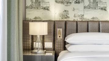 Habitación de hotel con una cama, una mesita de noche con lámpara y una pared con un mural de paisaje urbano.