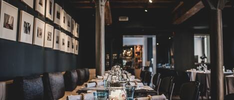 Un restaurante con una larga mesa lista para comer, cuadros en la pared y un techo de madera rústica.