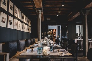 Un ristorante con un lungo tavolo apparecchiato per la cena, quadri alle pareti e un rustico soffitto in legno.