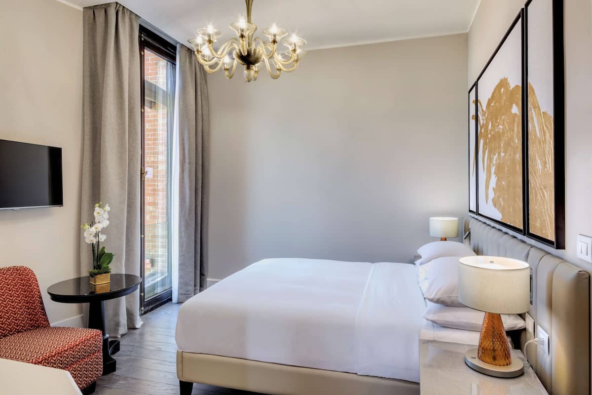 Une chambre d’hôtel avec un grand lit, un téléviseur fixé au mur, un lustre, une petite table avec une plante et un canapé.
