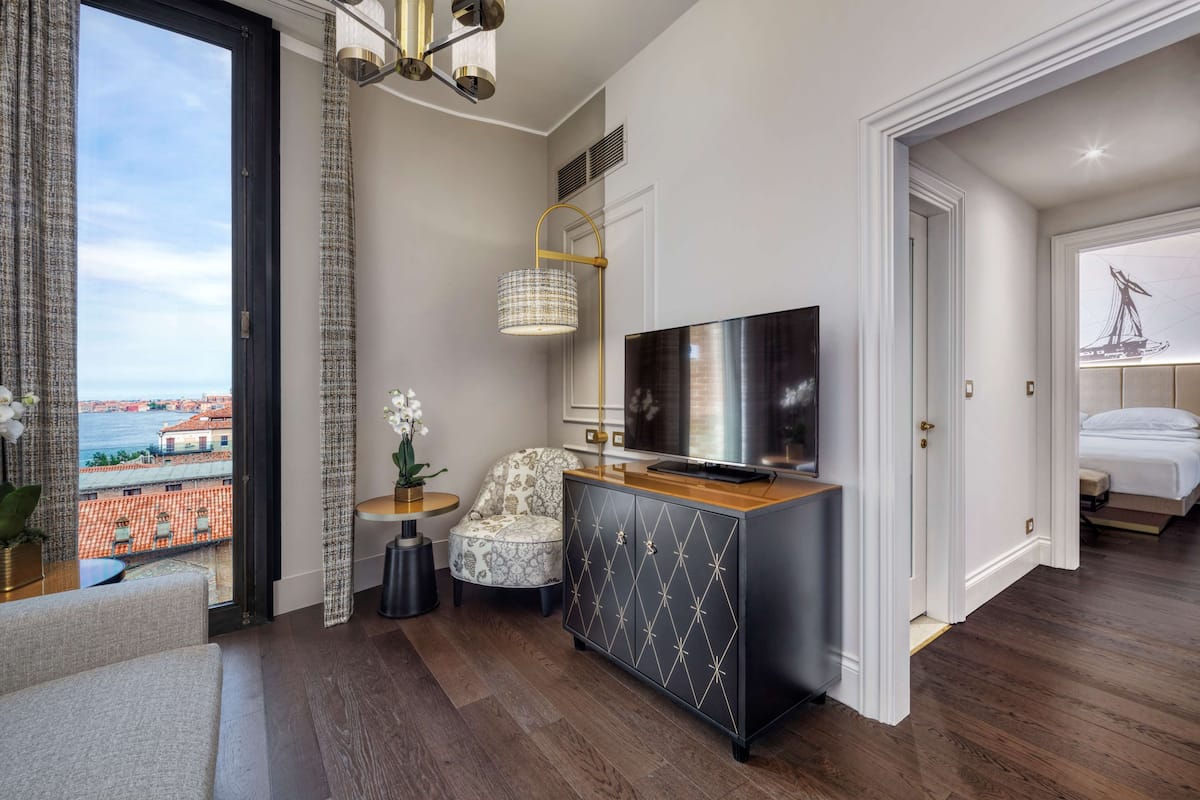 Une chambre d’hôtel moderne dotée d’une grande fenêtre, d’un téléviseur à écran plat, d’un fauteuil à motifs et d’une armoire en bois.