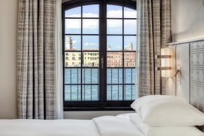 A hotel room with a large window offering a view of a cityscape and water. - Hilton Molino Stucky Venice (Venice)