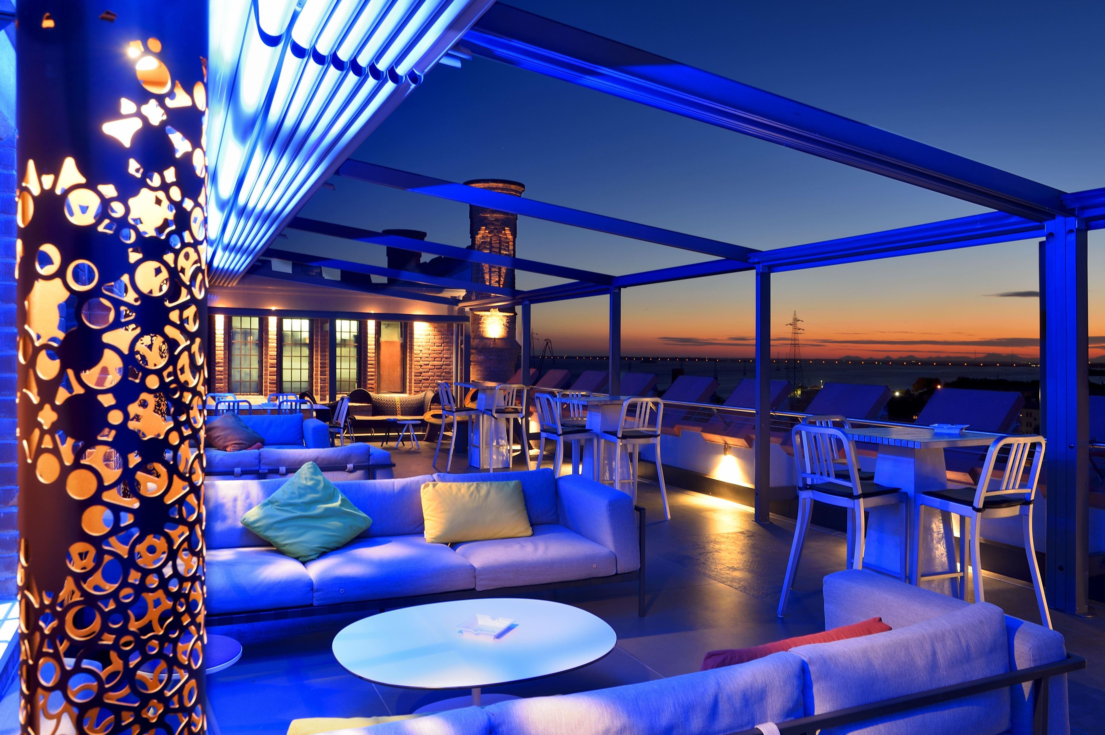 Una terrazza panoramica con posti a sedere e tavoli, un muro in mattoni e vista sul tramonto.