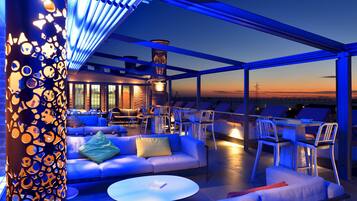 Una terrazza panoramica con posti a sedere e tavoli, un muro in mattoni e vista sul tramonto.