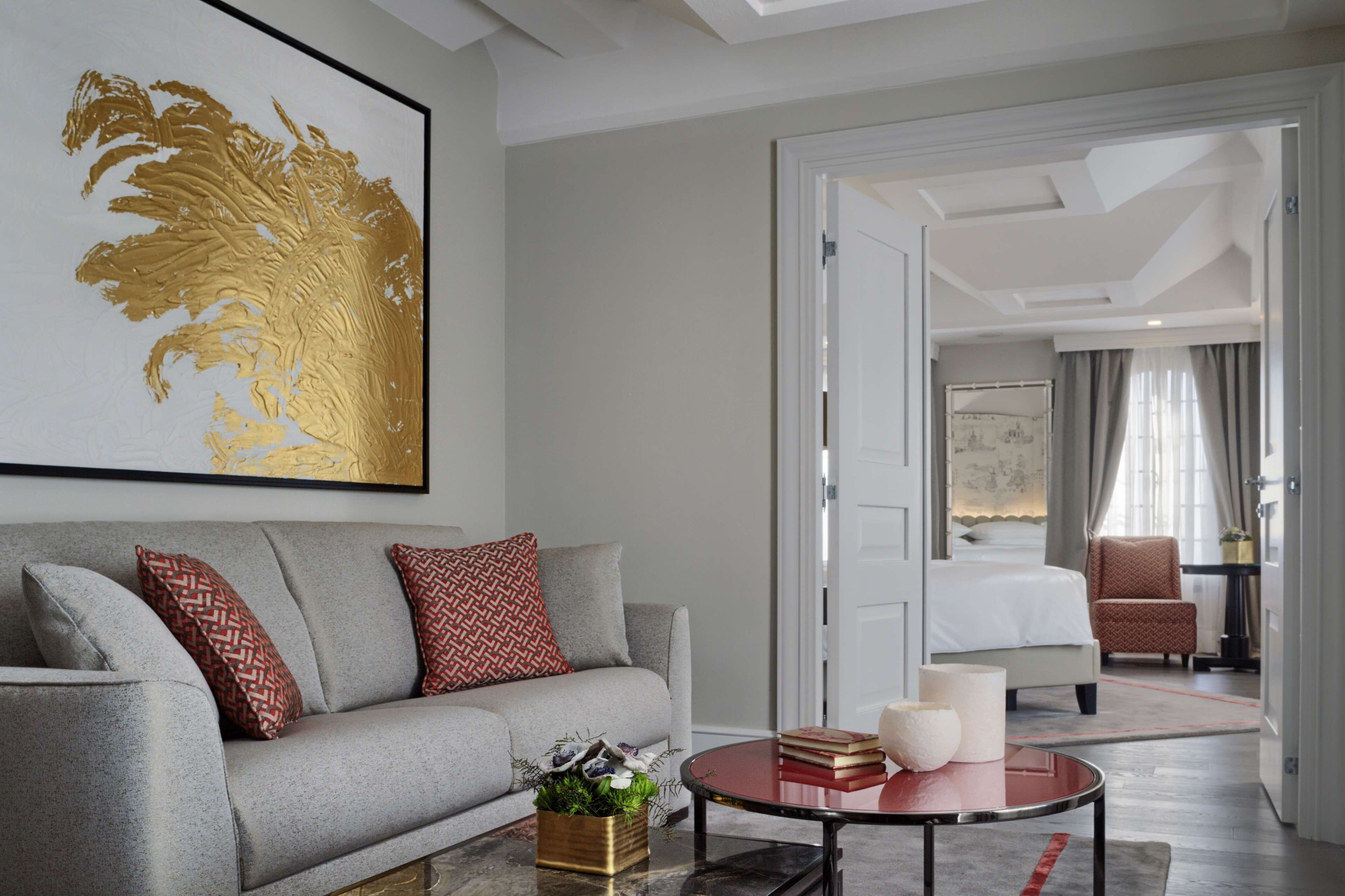 A modern hotel room with a grey sofa, a round coffee table, and a large framed artwork on the wall.