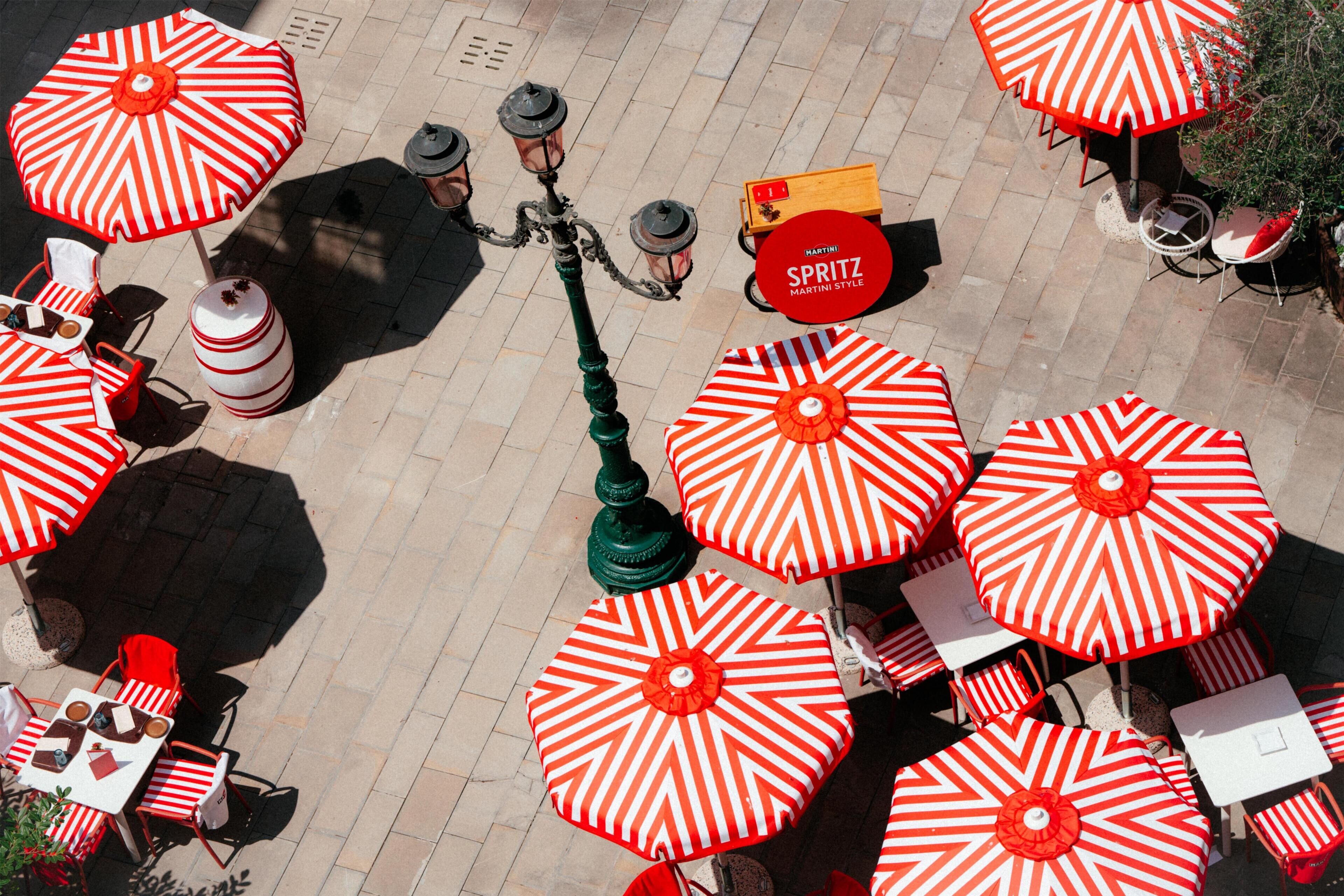 An outdoor seating area with red and white striped umbrellas, tables, and chairs.