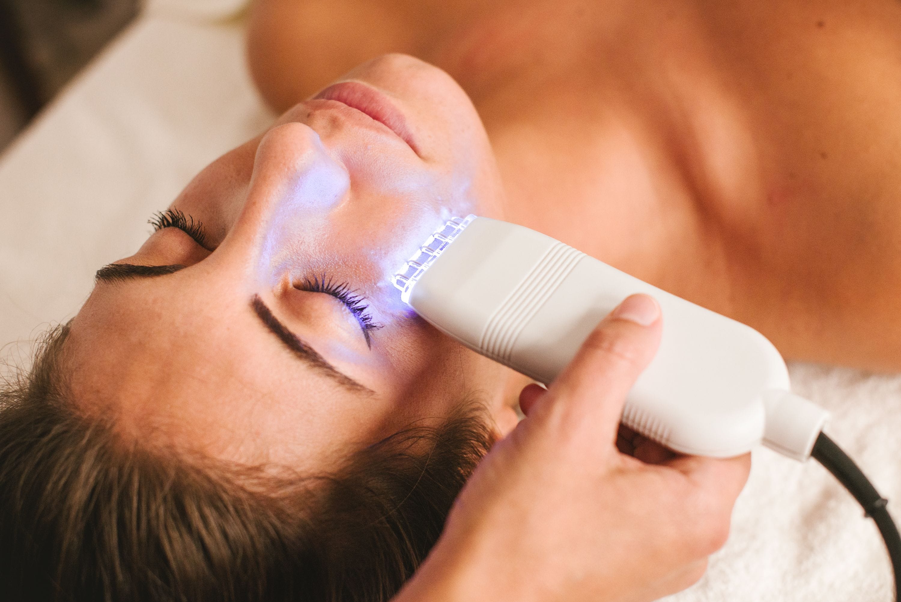 Una persona recibiendo un tratamiento facial con un aparato que emite luz.