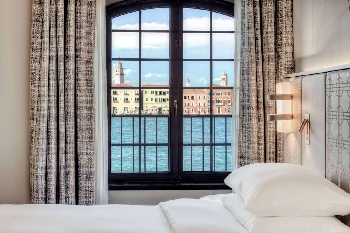 Une chambre d’hôtel dotée d’une grande fenêtre donnant sur un paysage urbain et sur l’eau.