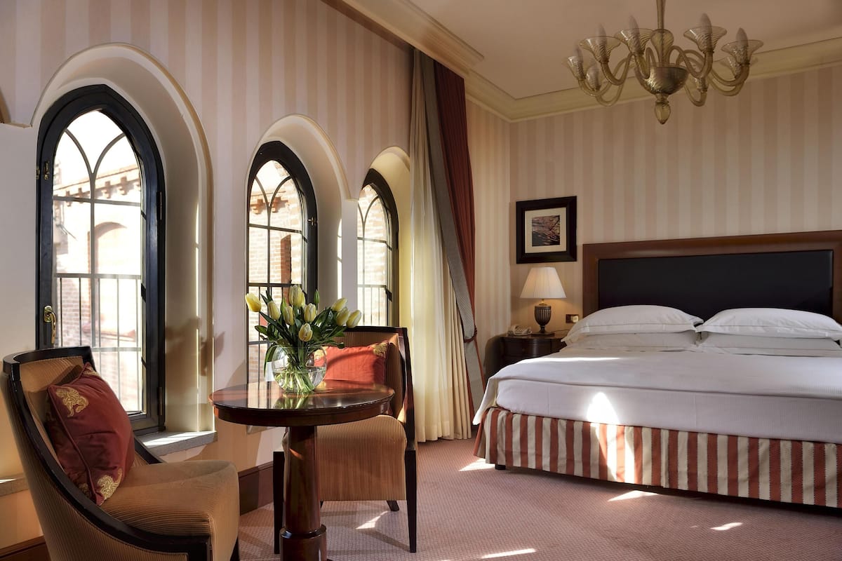 Une chambre d’hôtel avec un grand lit, une table ronde entourée de chaises et un lustre.