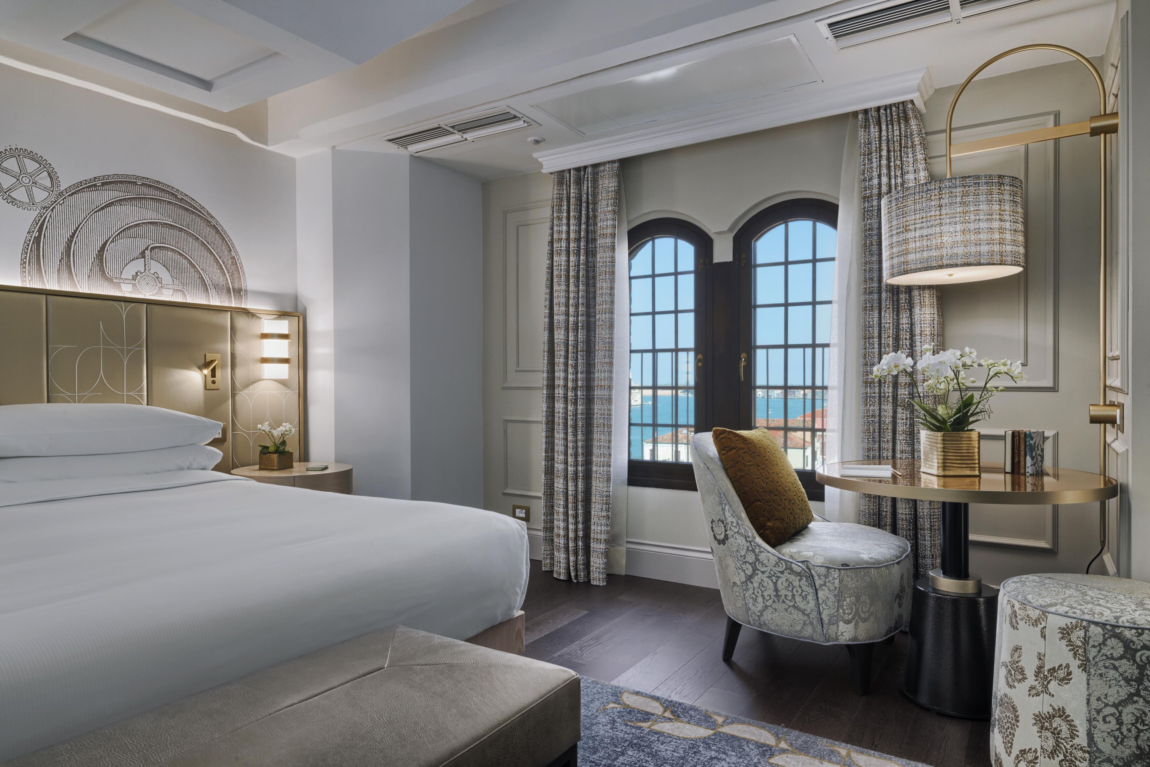 Ein Hotelzimmer mit einem großen Bett, einer Sitzecke mit einem Sessel, einem kleinen Tisch und Meerblick durch ein Fenster.