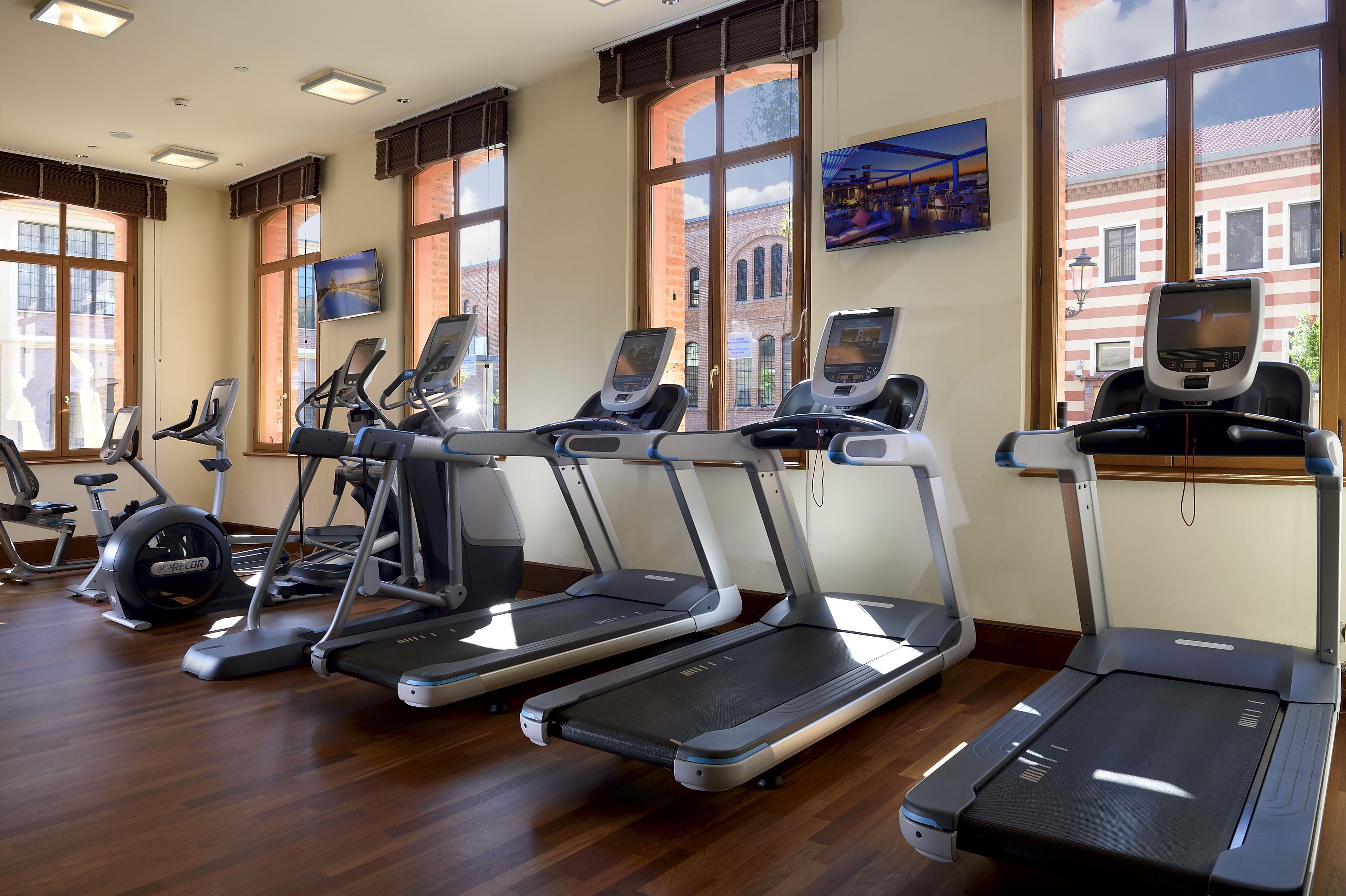 A gym with multiple treadmills, exercise bikes, and a television screen.