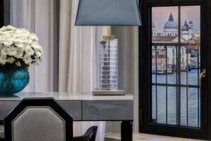 Una scrivania con un vaso di fiori bianchi, una lampada e vista sulla città attraverso una finestra.