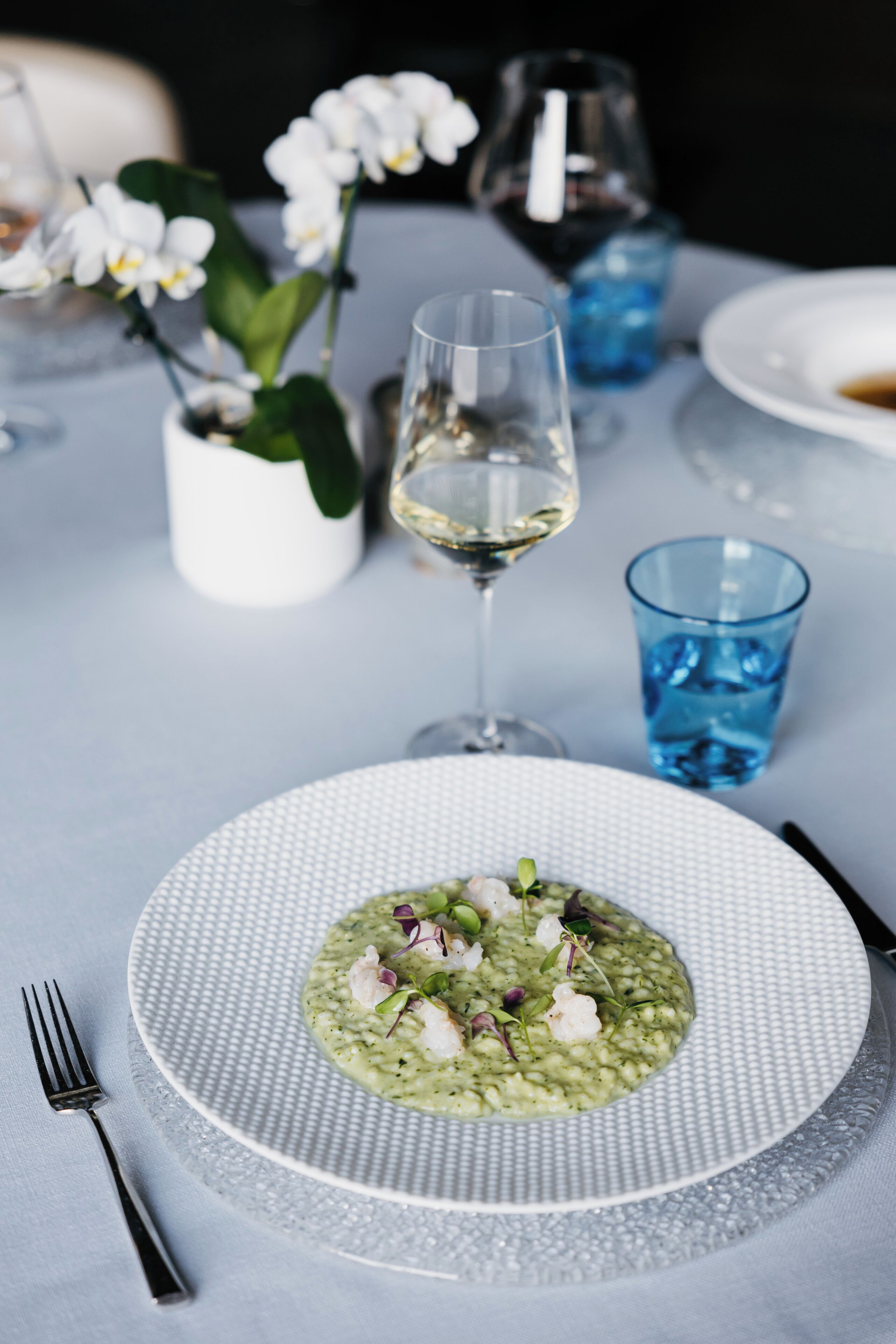 A dining table with a plate of food, a glass of white wine, and a blue glass.