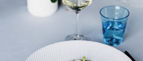 A dining table with a plate of food, a glass of white wine, and a blue glass.